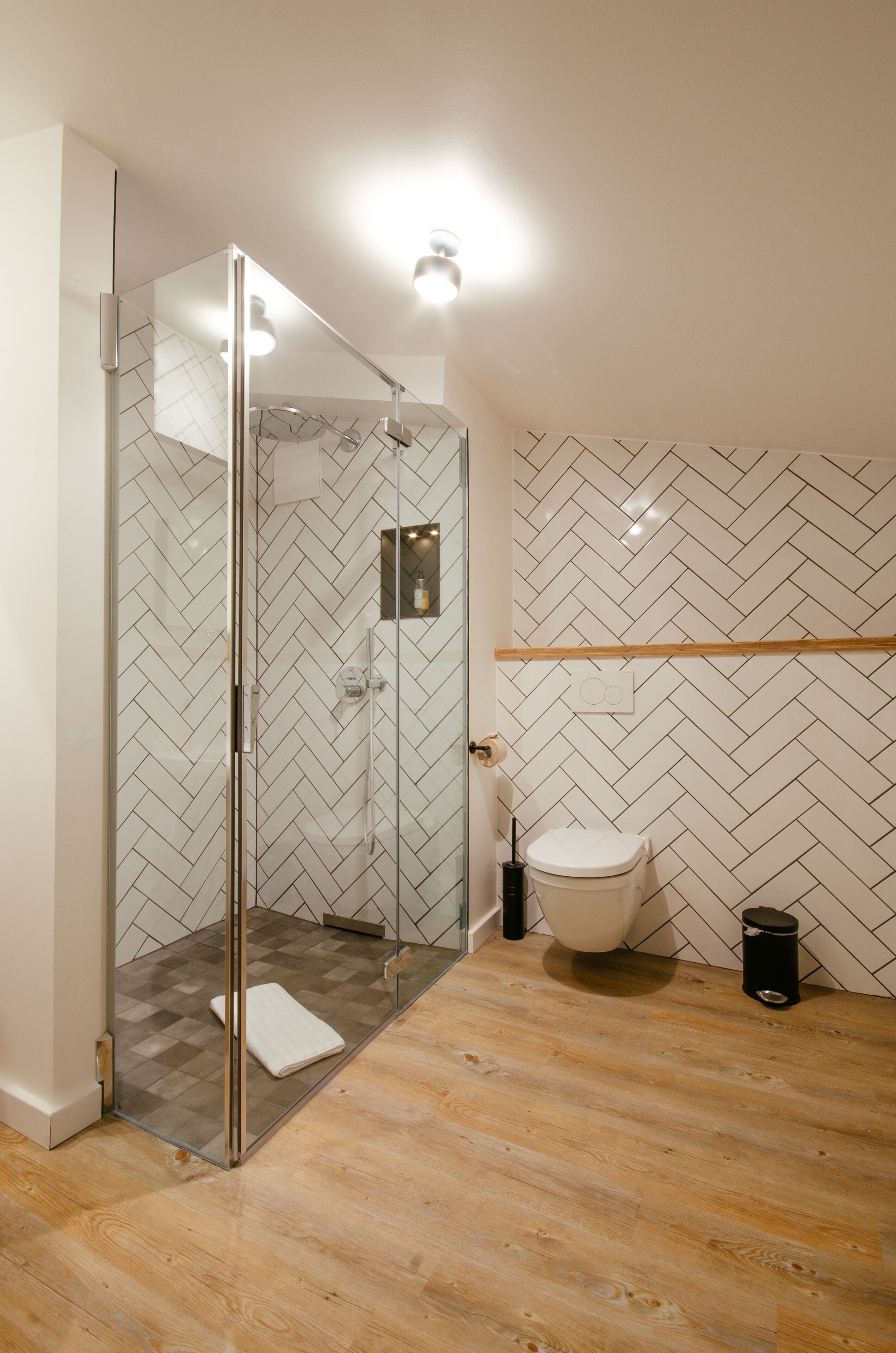 Een moderne badkamer met een douchecabine van glas, een wit toilet en een betegelde muur met een herringbone-patroon.