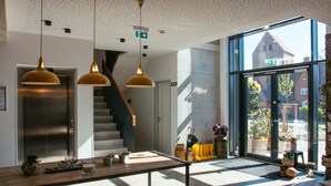 Un interior moderno con un mostrador de recepción de madera, una escalera y grandes ventanales que ofrecen vistas al exterior.