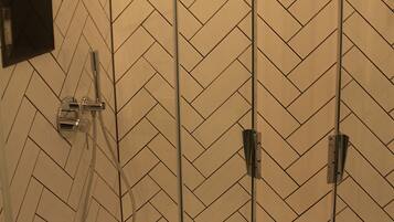 A glass-enclosed shower with a herringbone tile pattern on the walls.