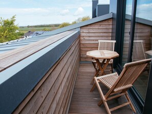 A wooden deck with a table and chairs, a glass wall, and a view of the countryside. - Hotel Landhafen (Niebuell)