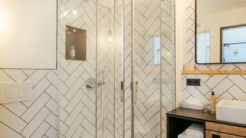 A modern bathroom with a glass-enclosed shower, a white toilet, and a wooden vanity with a mirror and shelves.