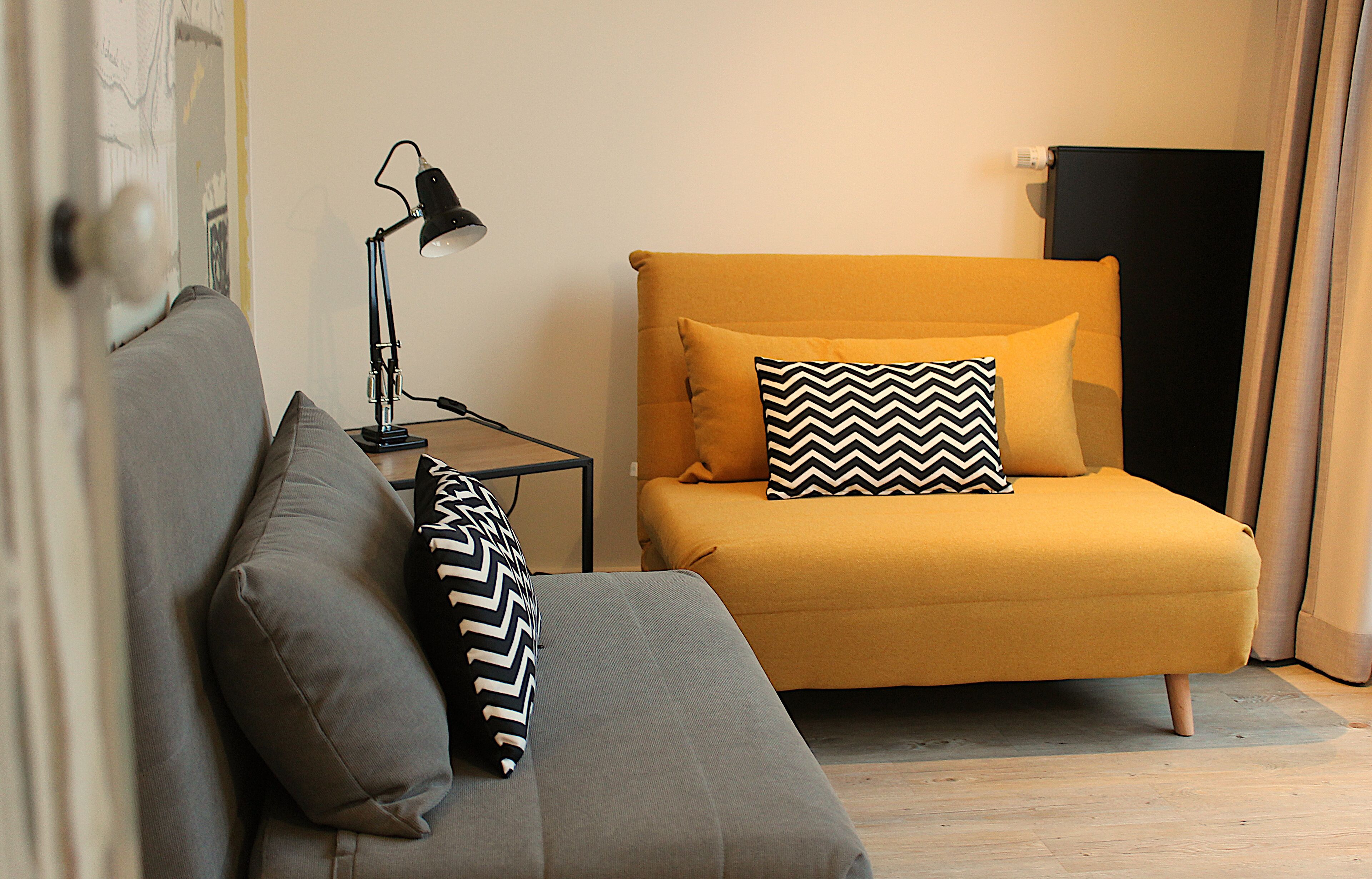Una habitación con un sofá, una mesita de noche con una lámpara y una cama con un cojín estampado.