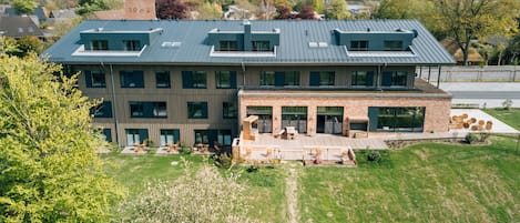 Un edificio moderno de varios pisos con techo plano, ventanas amplias y una terraza exterior espaciosa con mobiliario.