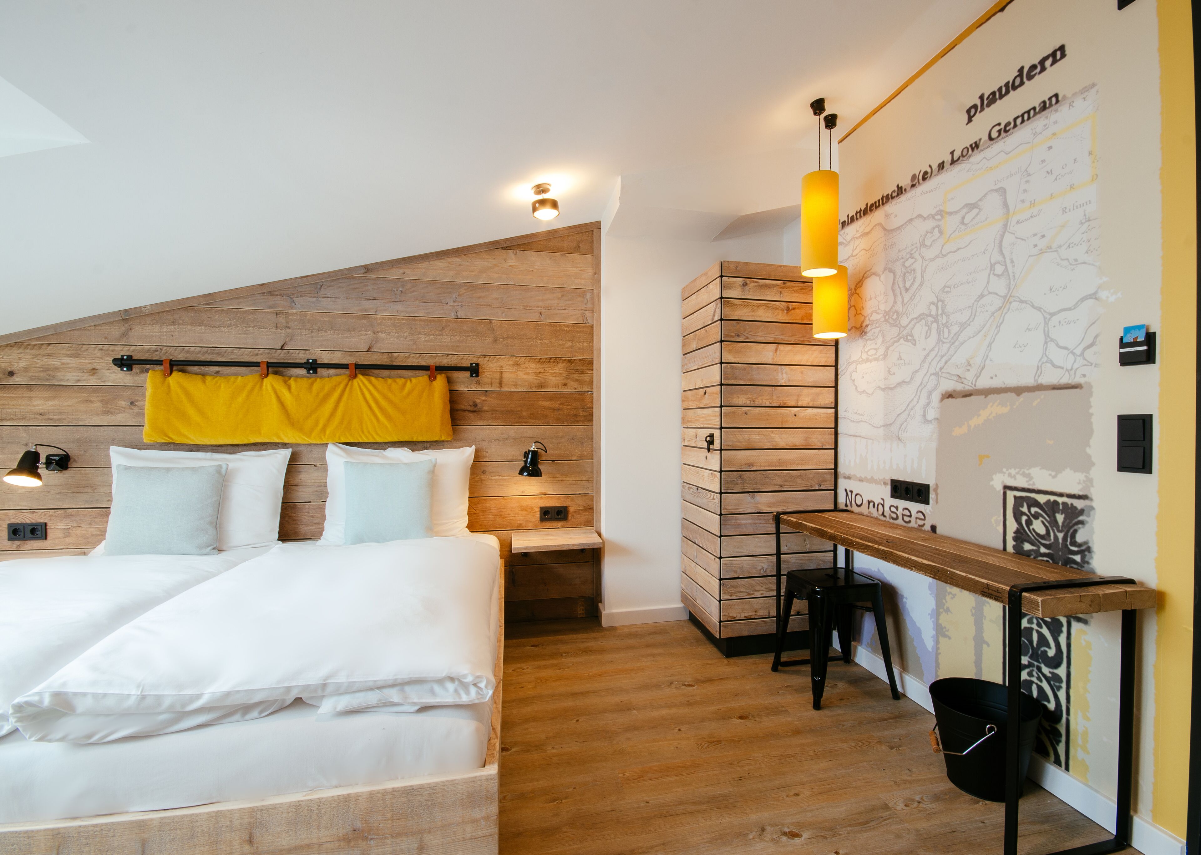 A bedroom with a wooden headboard, a bed with white linens, a yellow towel, a nightstand with a lamp, and a map on the wall.