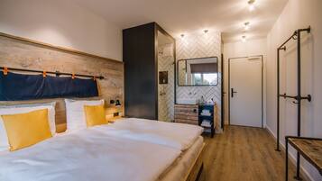 Una camera da letto moderna con una testiera in legno, un letto grande con biancheria da letto bianco e giallo, un armadio a muro e un bagno con rivestimento a mosaico a spina di pesce.