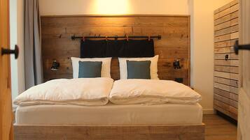 Una cama bien tendida con ropa blanca y dos almohadas, un cabecero de madera y una lámpara de pared.