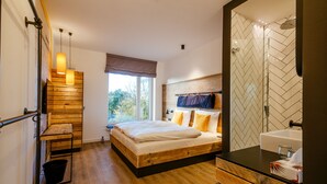 Un dormitorio moderno con una cama de madera, un ventanal grande y un baño con un revestimiento de baldosas en espiga.