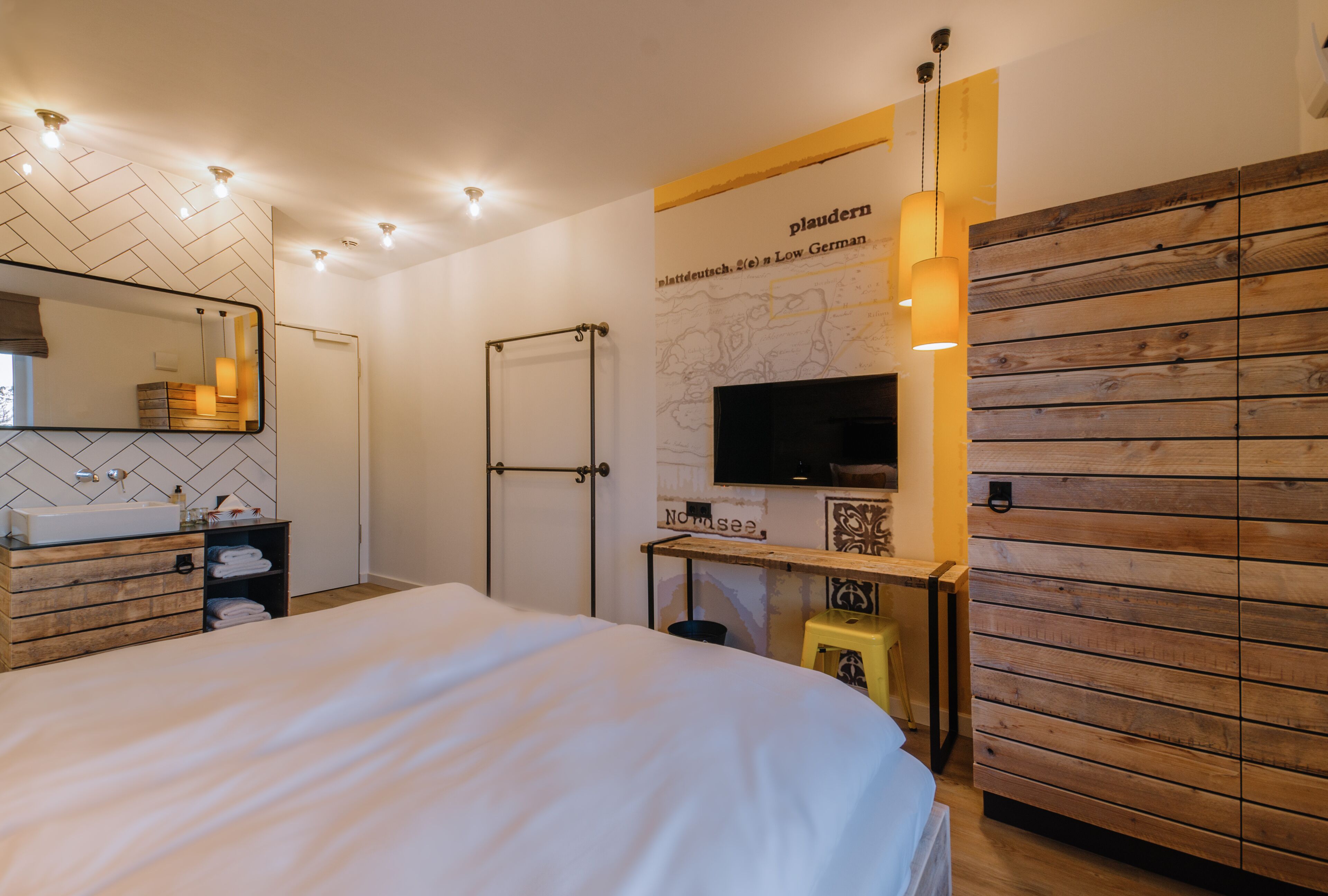 Ett modernt hotellrum med en stor säng, en träpanel på väggen, en väggmonterad TV och ett skrivbord i trä med en stol.
