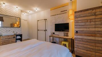 Ett modernt hotellrum med en stor säng, en träpanel på väggen, en väggmonterad TV och ett skrivbord i trä med en stol.