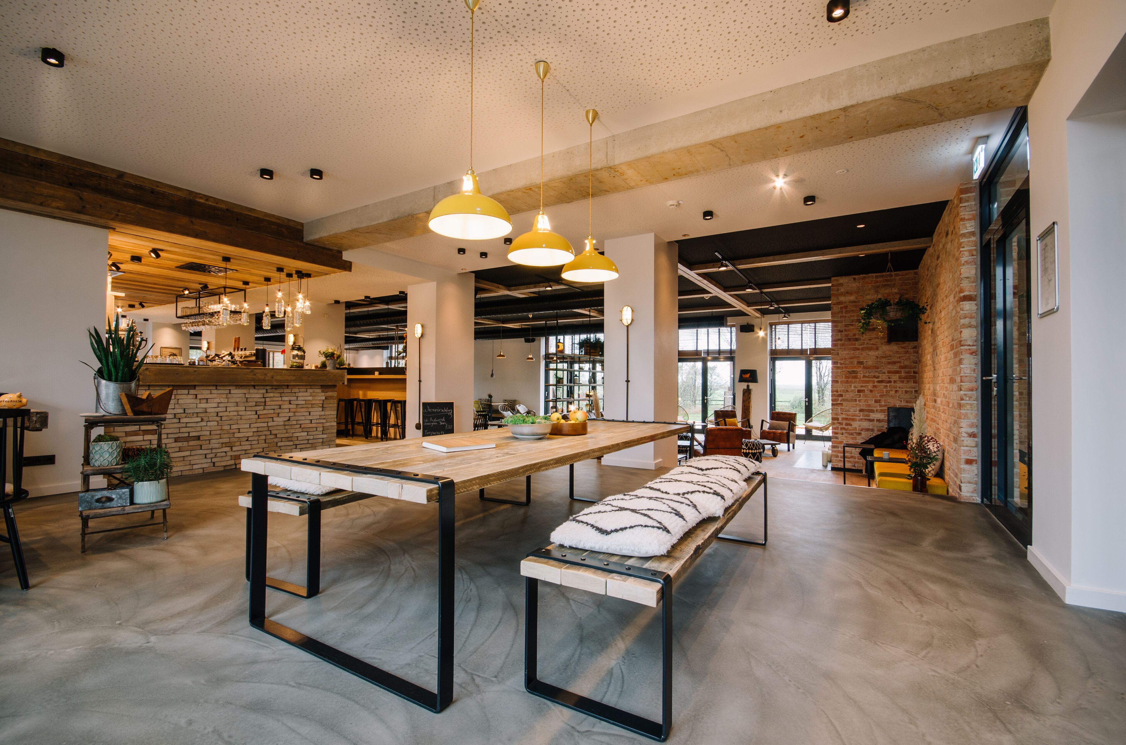 Een ruime, moderne keuken met een lange houten tafel, hangende pendantlampen en een accentmuur van baksteen.