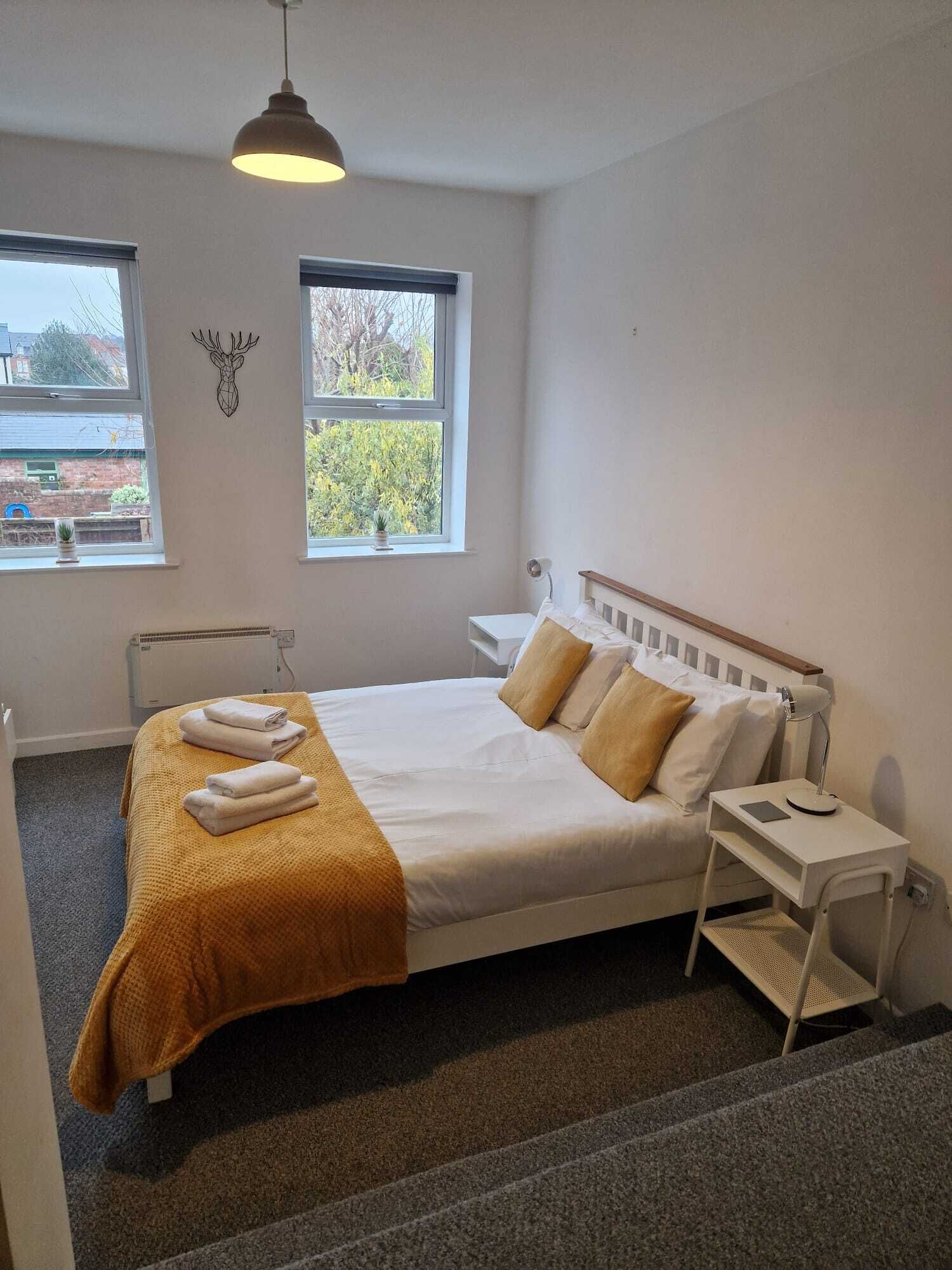 Une chambre à coucher avec un lit, une table de chevet, une lampe et une fenêtre donnant sur des arbres.