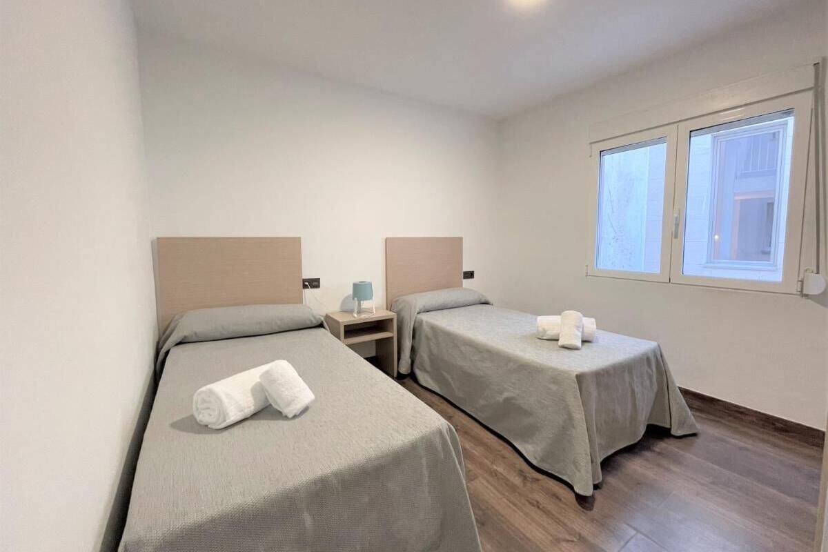 A hotel room with two single beds, a nightstand, a table, and a window with curtains.