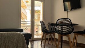 A room with a sofa, a dining table with chairs, a TV mounted on the wall, and a sliding glass door leading to an outdoor balcony. - L&G Apartamentos (Benidorm)
