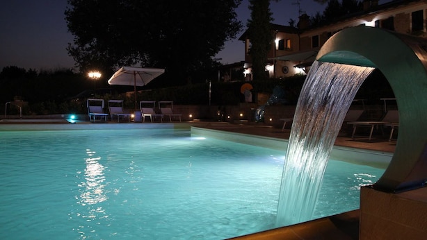 Una piscina con una cascada, sillas de descanso y un edificio al fondo.