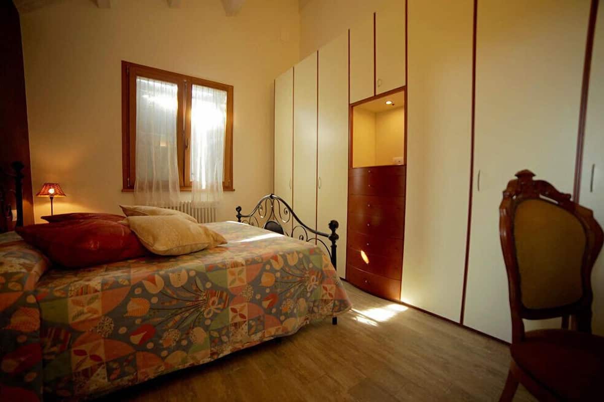 Quarto com cama, cadeira, guarda-roupa e janela com cortinas.