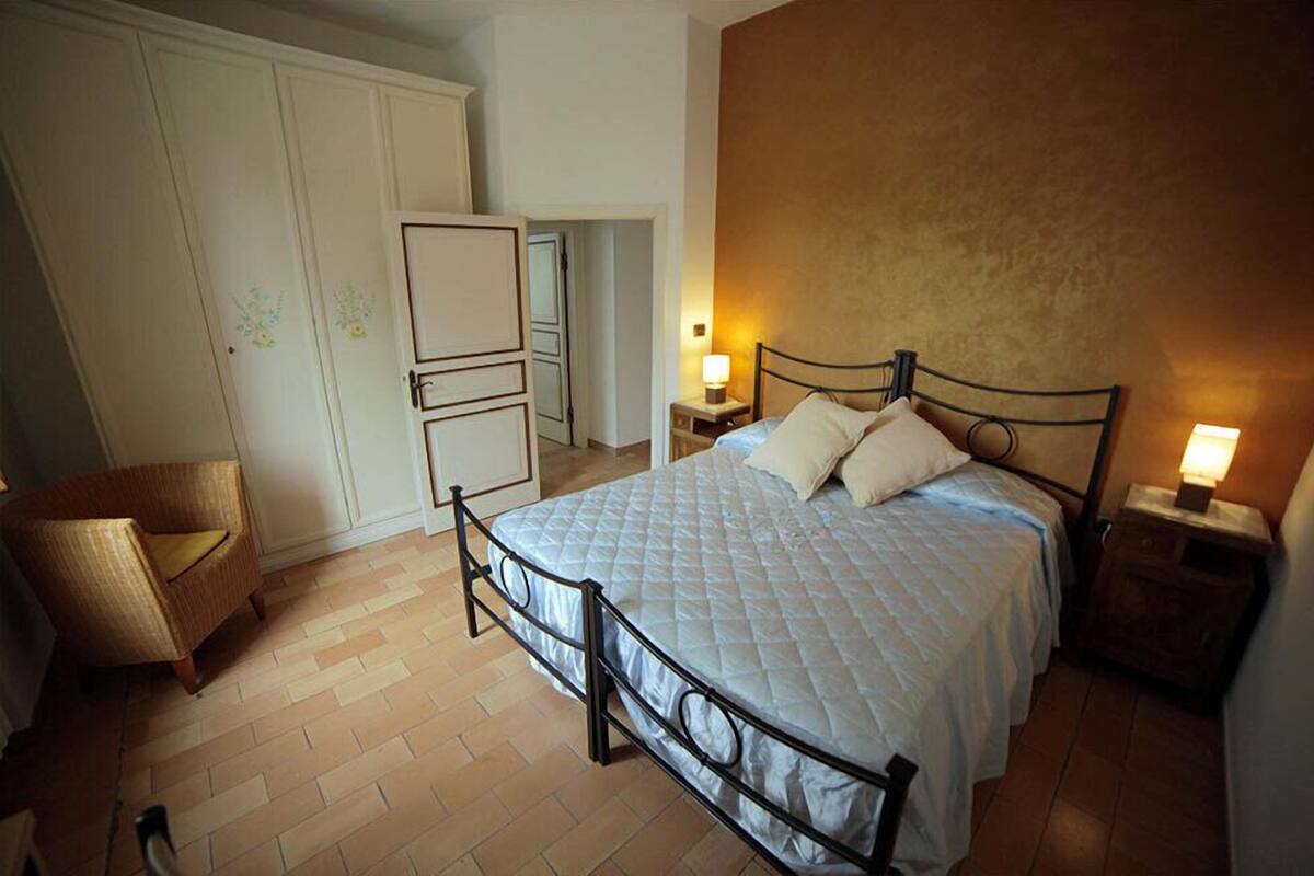 Quarto com uma cama, uma cadeira, um guarda-roupa e uma mesa de cabeceira com abajur.