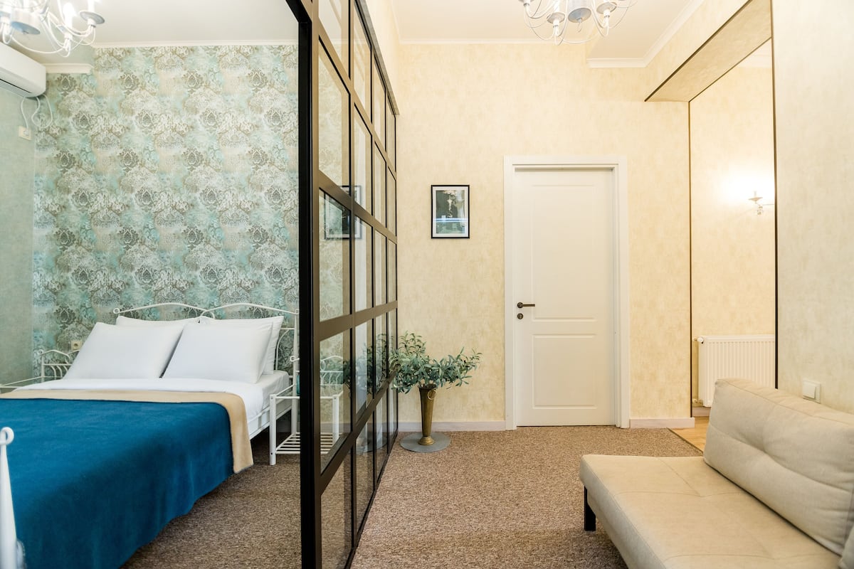 A bedroom with a bed, a sofa, a potted plant, and a door.
