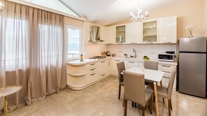 Een moderne keuken met witte kasten, een eethoek met tafel en stoelen, een koelkast en een kroonluchter.