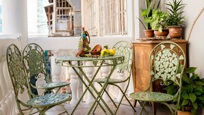 Een balkon met een tafel voor twee personen, omringd door groene metalen stoelen, een houten kast met potplanten en een uitzicht op gebouwen op de achtergrond.