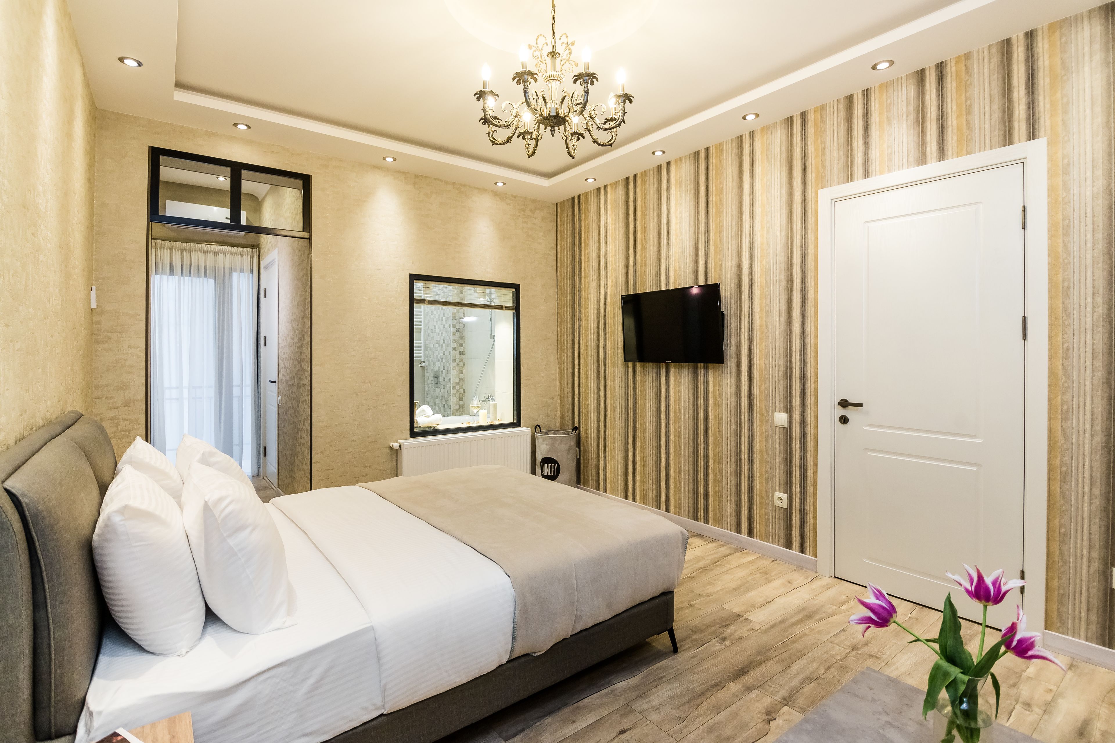 Une chambre moderne avec un grand lit, un lustre, un téléviseur à écran plat et une porte.
