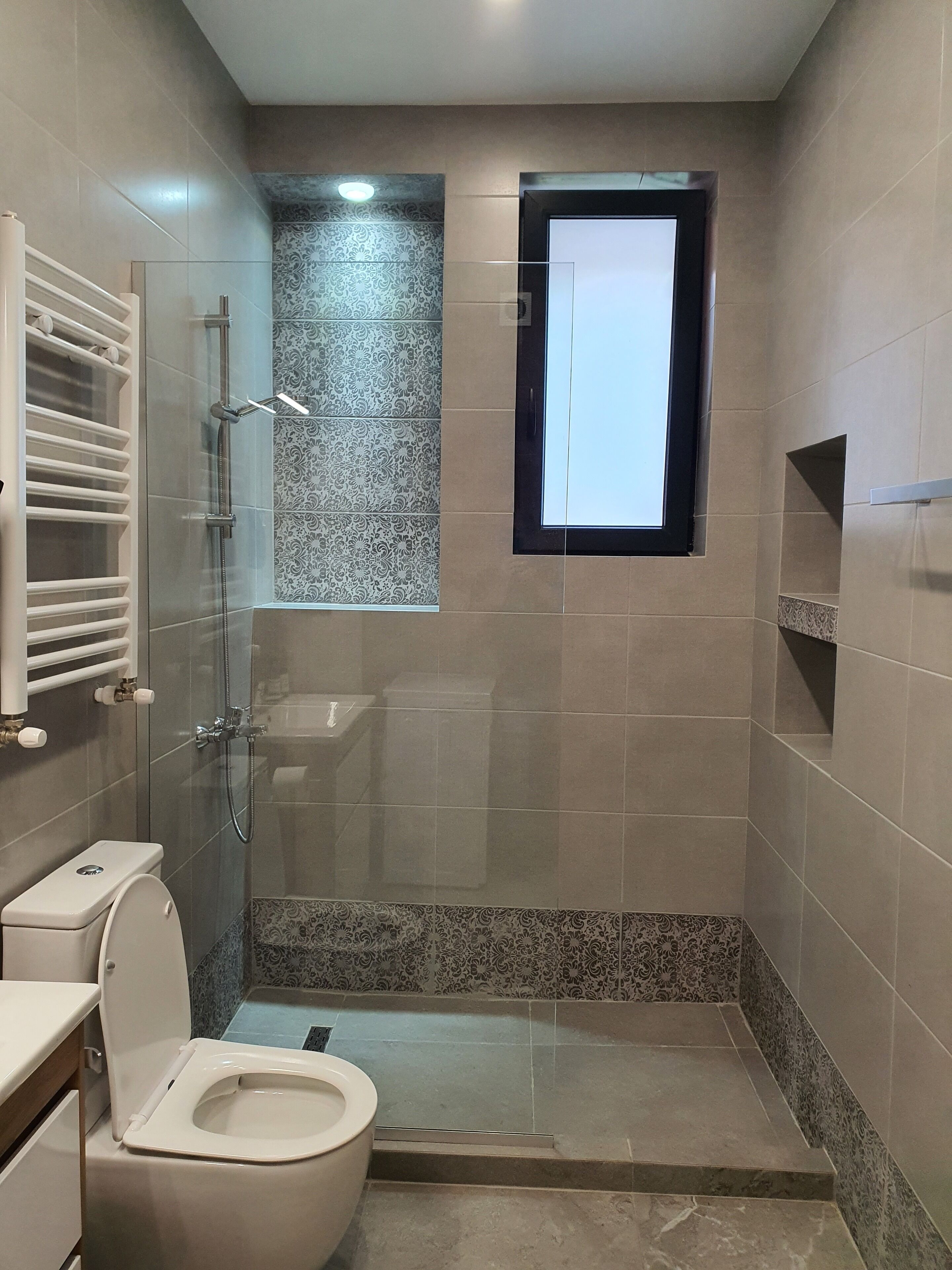 A modern bathroom with a glass-enclosed shower, a toilet, and a small window.