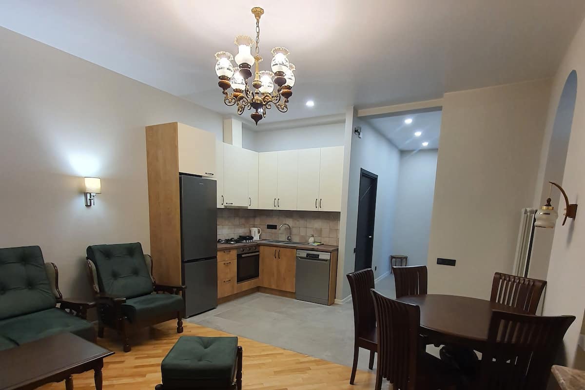 A modern living room with a dining area, wooden flooring, and a kitchen in the background.