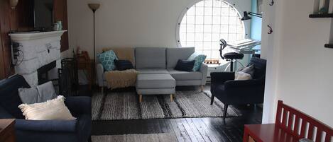 A living room with a grey sofa, a blue armchair, a red bench, and a large window.