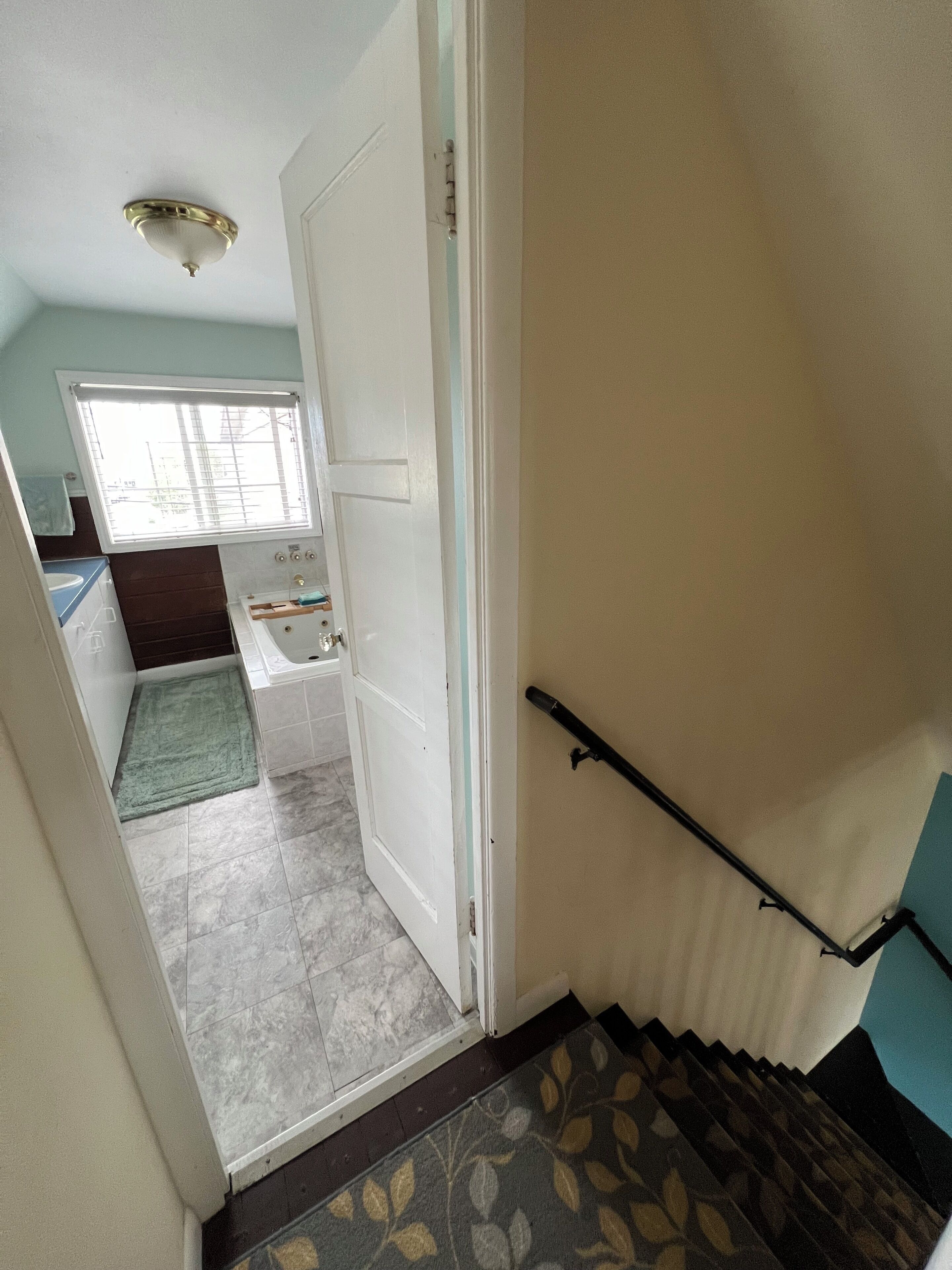 A staircase leading to a bathroom with a bathtub, a window with blinds, and a ceiling light fixture.