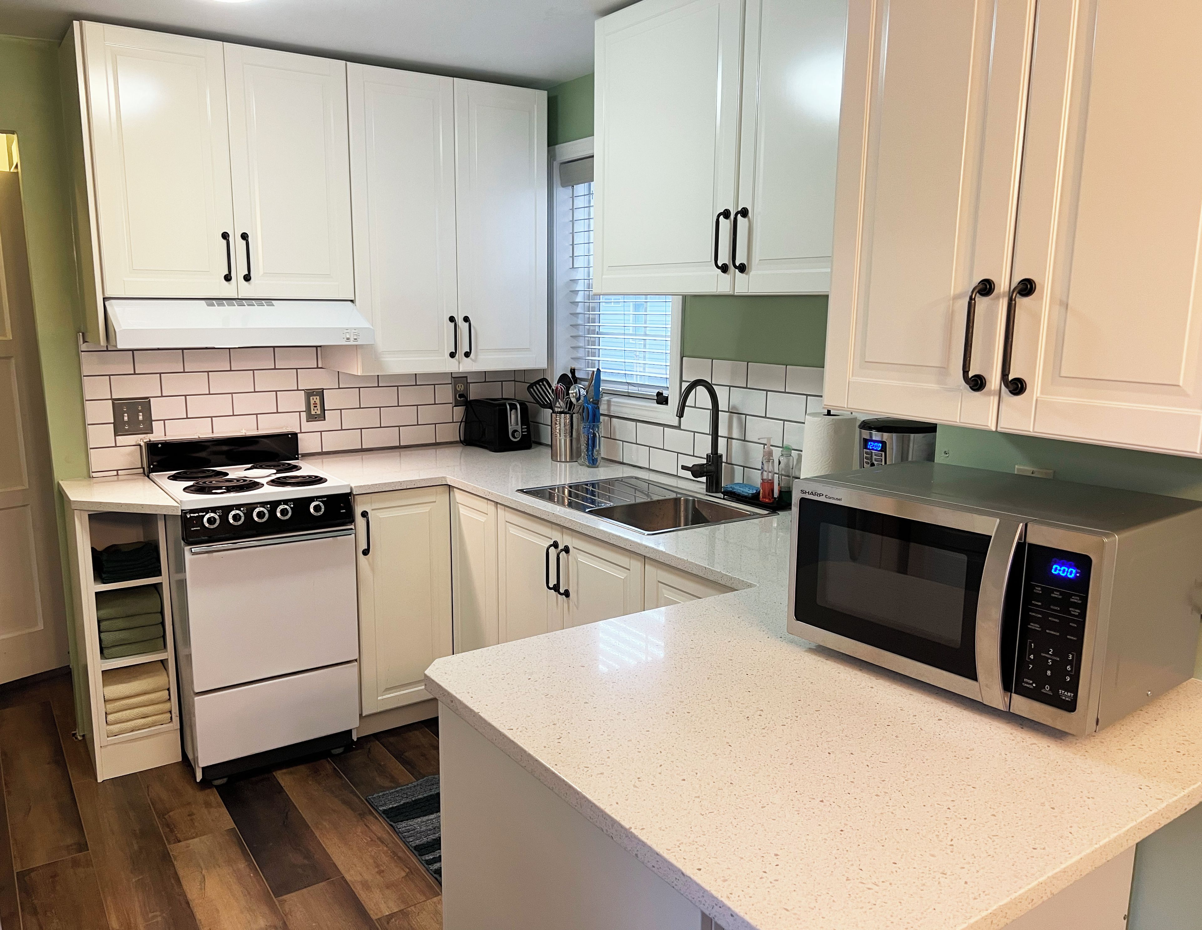 A kitchen with white cabinets, a stove, a microwave, and a sink.