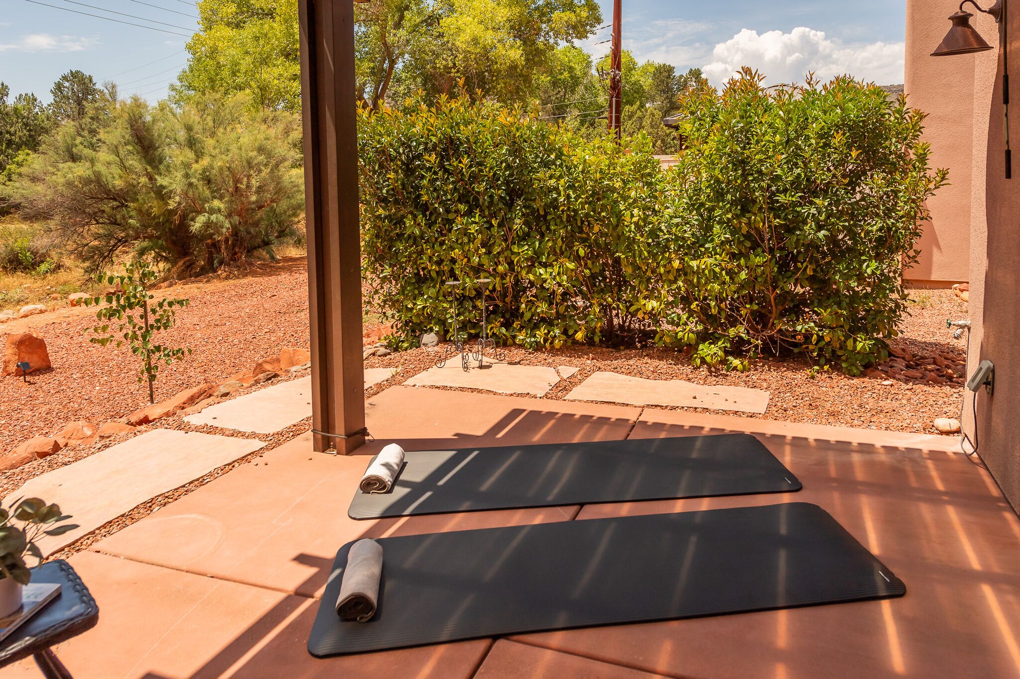 Eine Terrasse im Freien mit zwei Yogamatten, einem kleinen Tisch mit einer Pflanze und einer Wandleuchte.