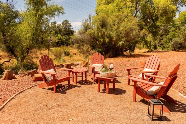 Een terras met Adirondack-stoelen en een tafel, omringd door grind en bomen.