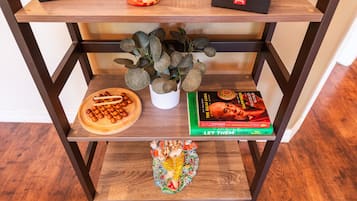 Ein Holzregal mit einer Pflanze, einer Holztablett mit runden Gegenständen, einem Buch mit dem Titel 'The Dalai Lama' und einem dekorativen Gegenstand.