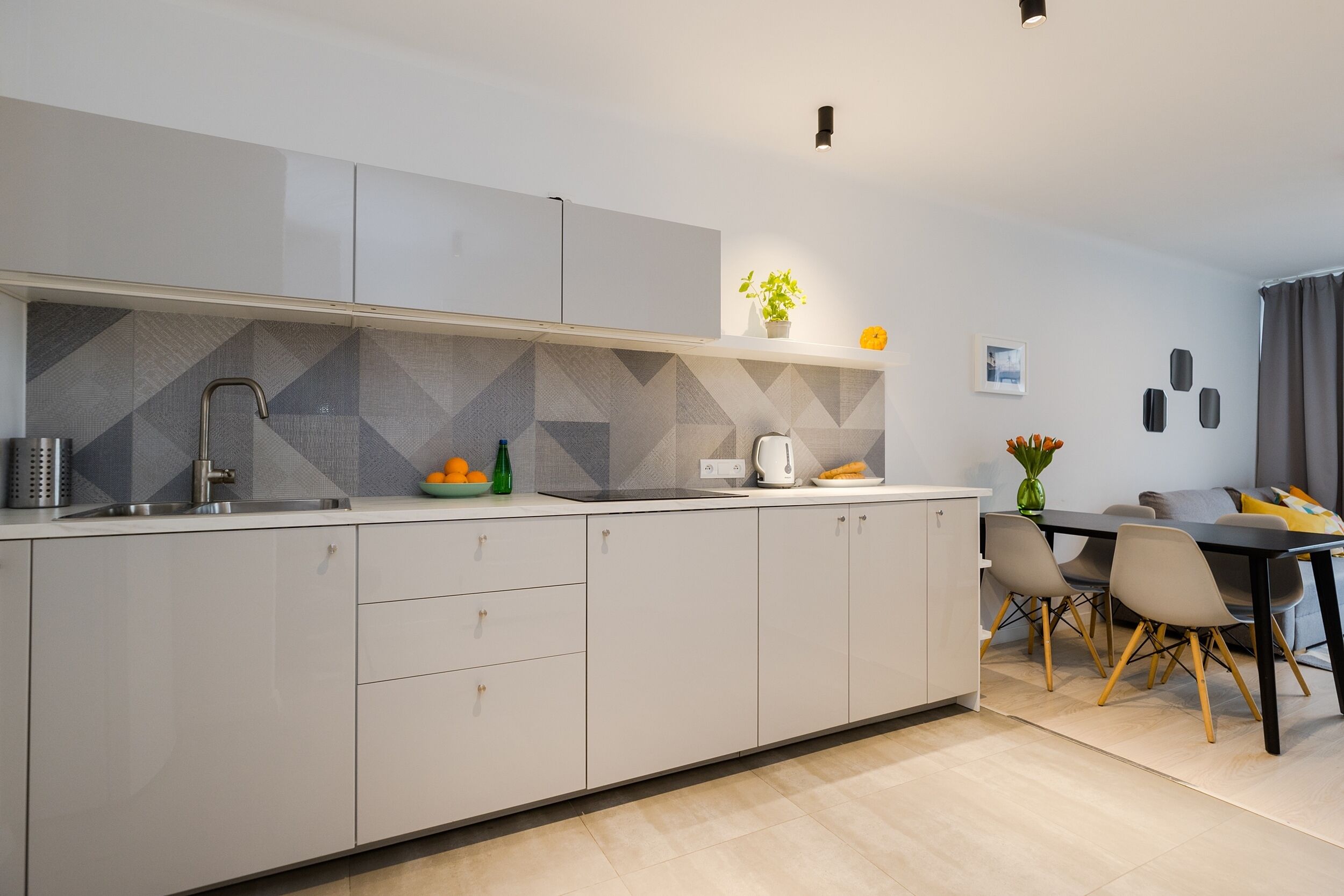 A modern kitchen with a built-in sink, a dining area with a table and chairs, and a potted plant on the counter.