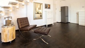 Eine moderne Küche mit dunklem Holzboden, einem braunen Ledersessel, einem weißen Schrank und einem Edelstahlkühlschrank.