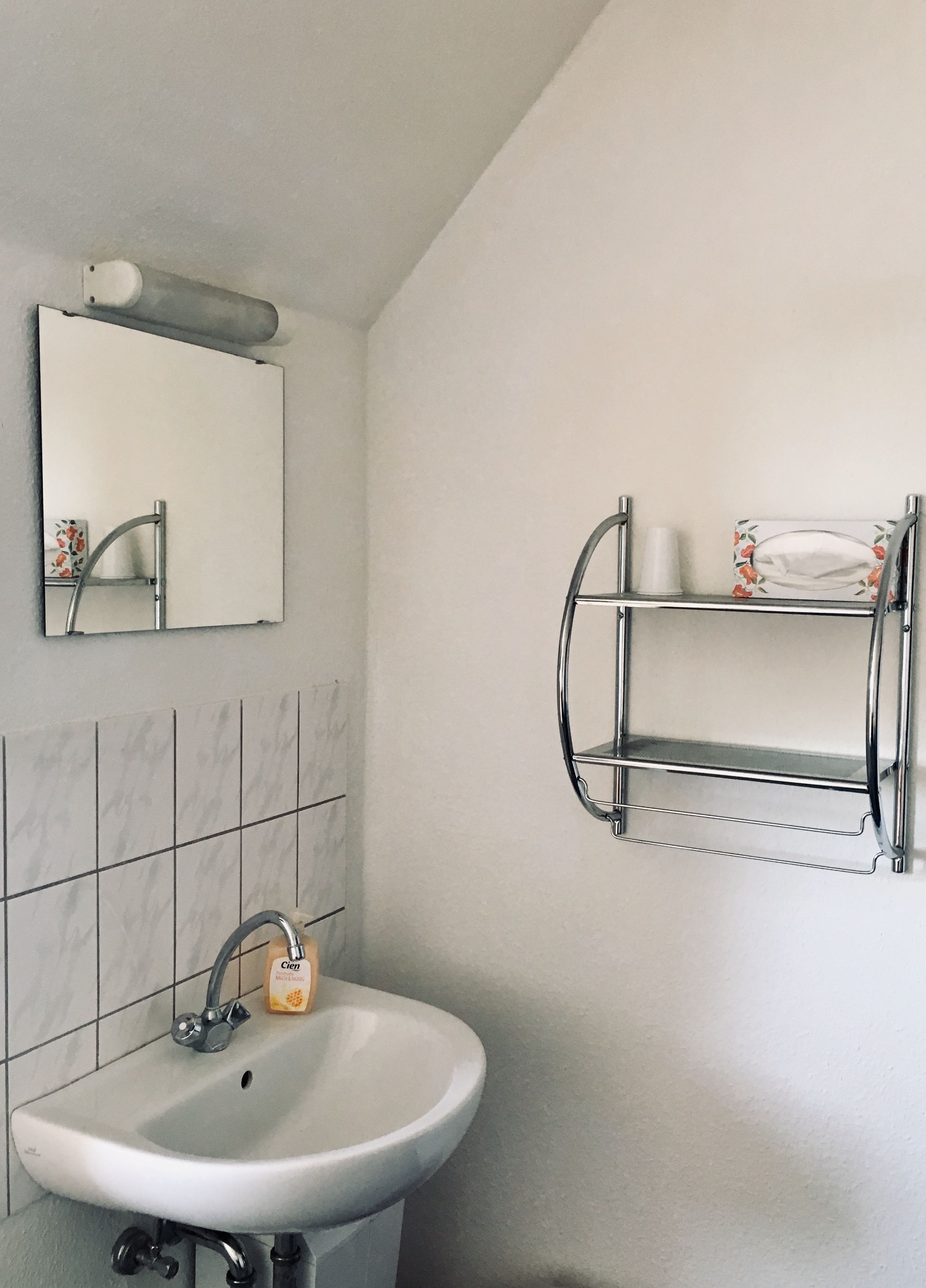 Ein Badezimmer mit einem weißen Waschbecken, einem Spiegel und einem chromfarbenen Handtuchhalter.