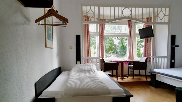 A room with a bed, a desk, a chair, a TV, and a window with curtains.