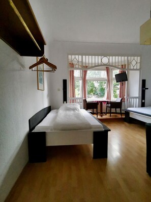 Una habitación con cama, escritorio, silla, televisión y ventana con cortinas.