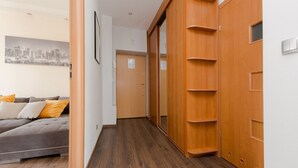 A hallway with a wooden wardrobe, a grey sofa with yellow cushions, and a cityscape painting on the wall. - ShortStayPoland Staszica B76 (Warsaw)