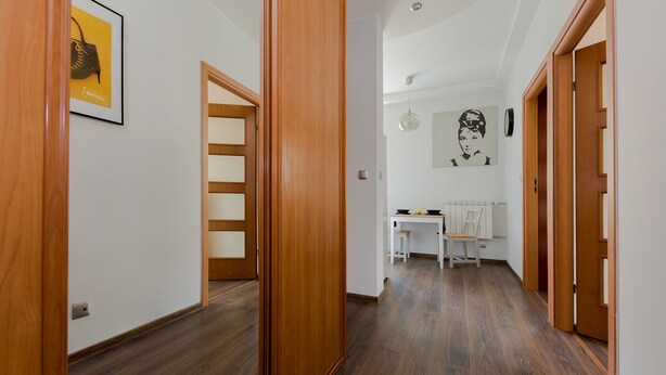 A hallway with wooden flooring and doors, leading to a dining area with a table and chairs. - ShortStayPoland Staszica B76 (Warsaw)