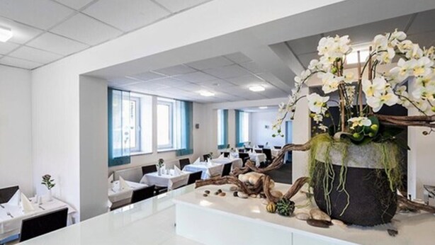 Een moderne hotellobby met een centraal receptiebalie, meerdere zithoeken en een decoratieve plantenpresentatie.