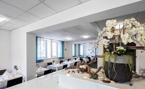 A modern hotel lobby with a central reception desk, multiple seating areas, and a decorative plant centerpiece. - Hotel City Oase Lb (Ludwigsburg)
