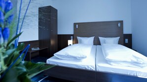 Een hotelkamer met een tweepersoonsbed, een houten hoofdbord, een nachtkastje met een lamp en een garderobe.