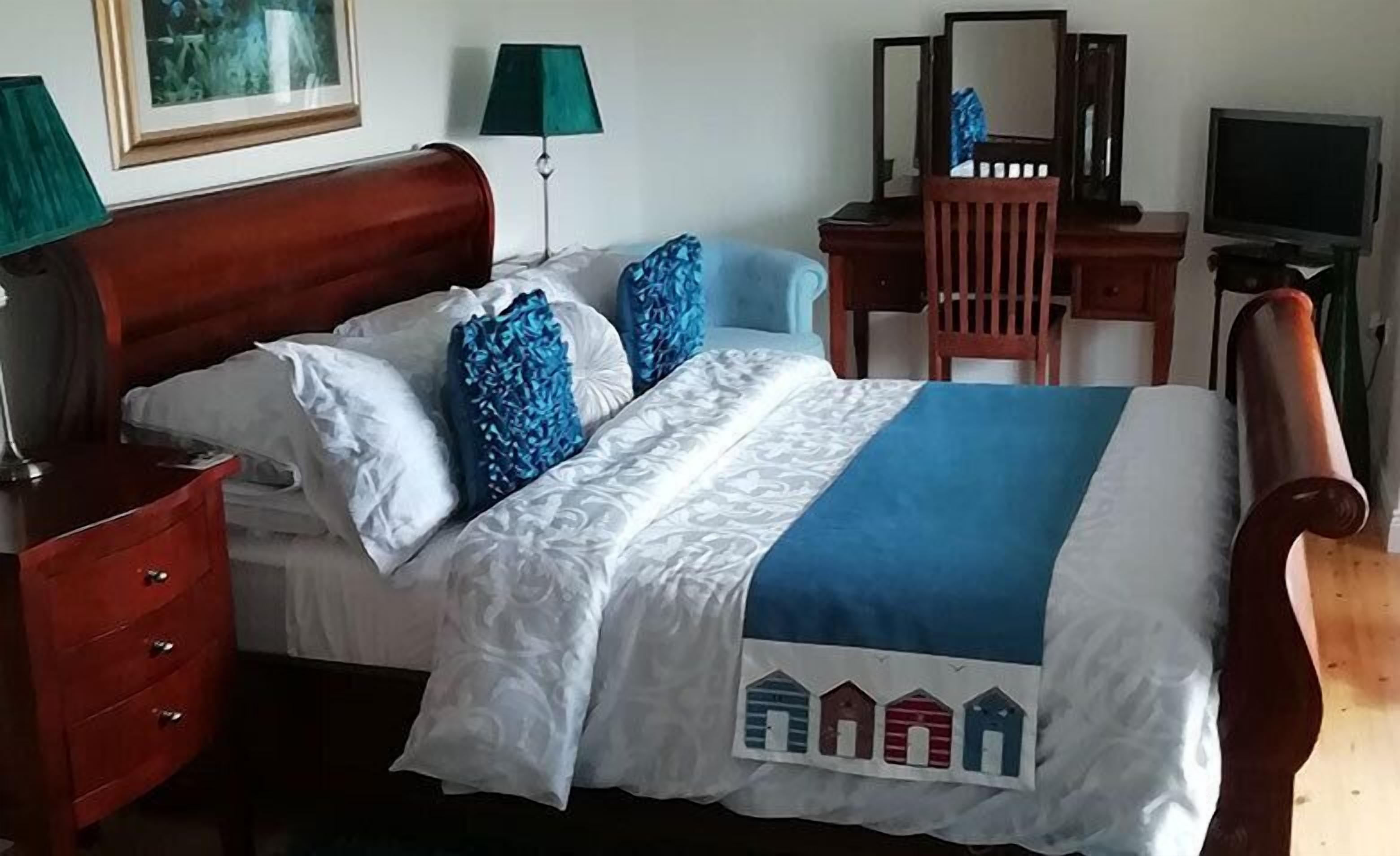 A neatly made bed with a blue and white bedspread, a wooden headboard, and a bedside table with a lamp.