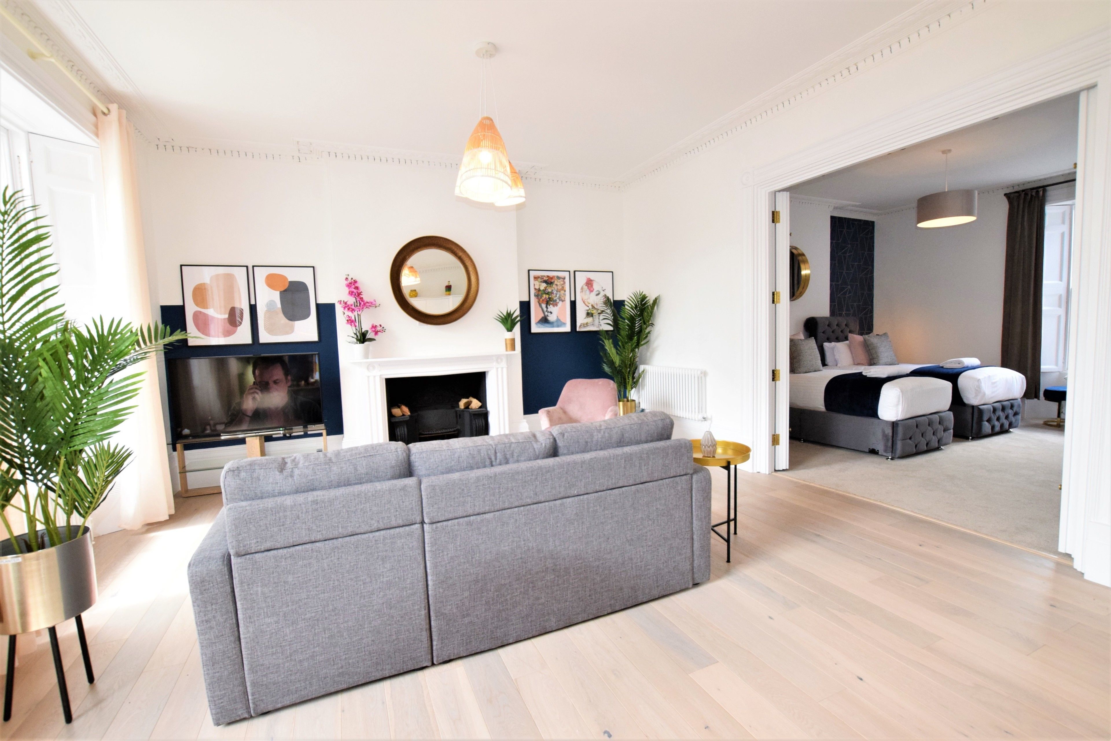 A modern living room with a grey sectional sofa, a fireplace, and a bed in the background.