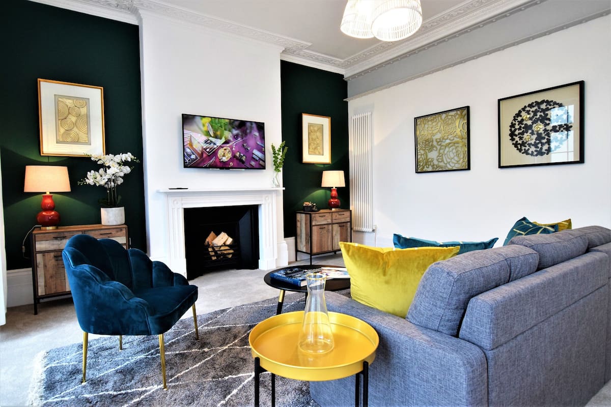 A modern living room with a fireplace, a blue armchair, a grey sofa, and a yellow side table.