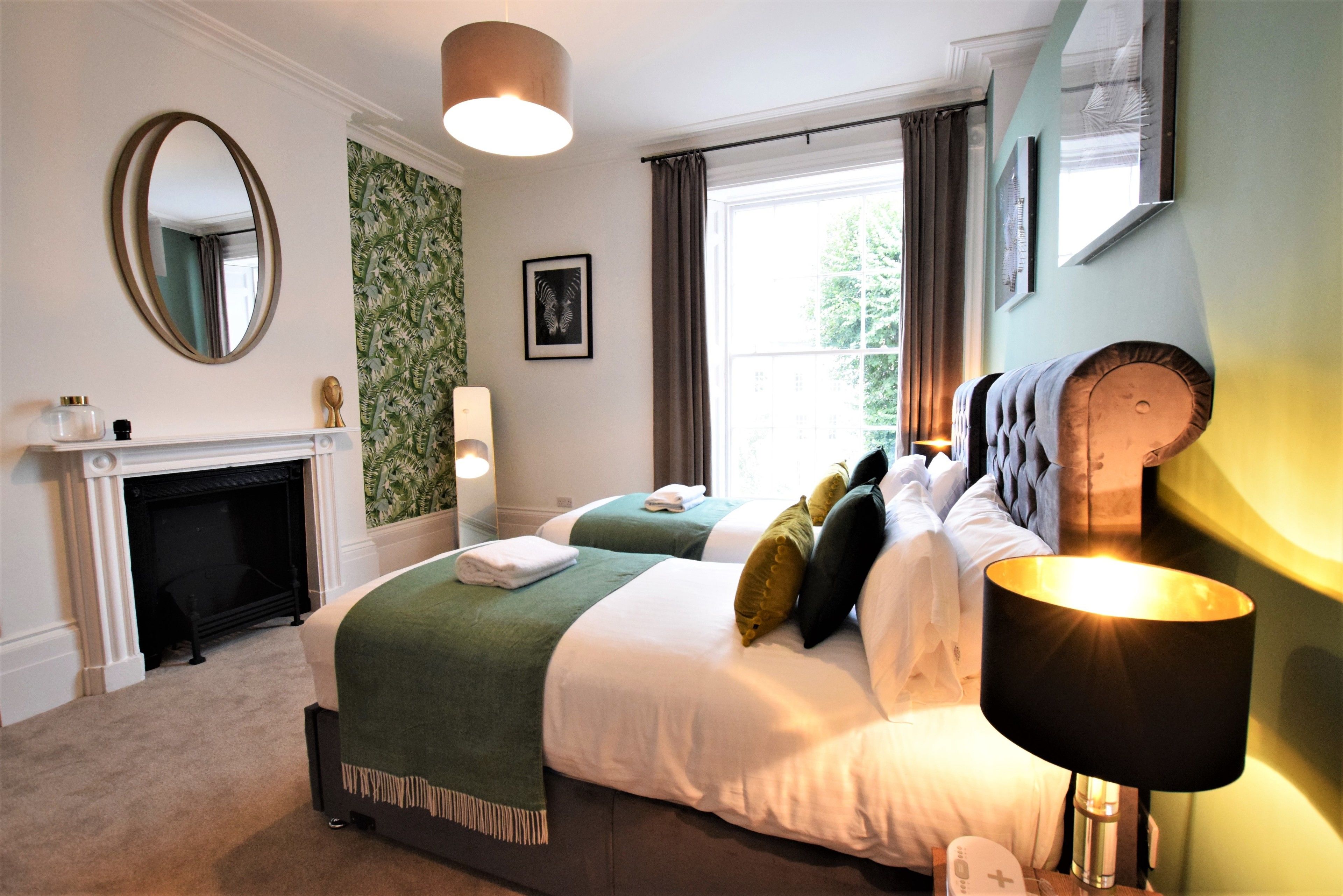 A hotel room with a large bed, a fireplace, a green wall, and a window with curtains.