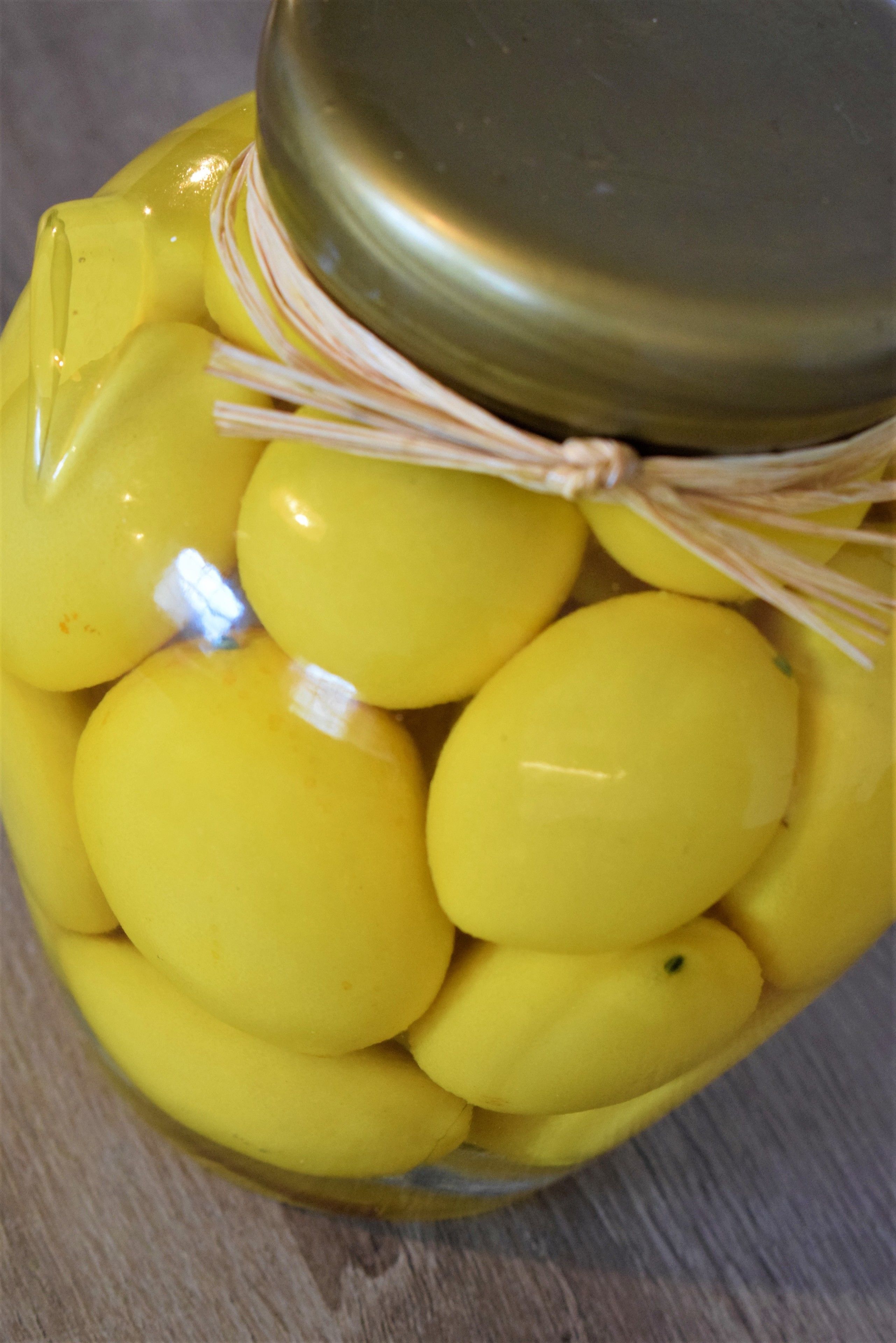 Un tarro lleno de objetos amarillos, posiblemente limones, cerrado con una tapa de metal y atado con un cordón.