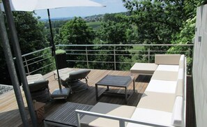 Eine Terrasse mit Gartenmöbeln, darunter eine Sitzecke und ein Tisch, umgeben von einem Metallgeländer.