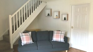 A living room with a grey sofa, two plaid pillows, a wooden staircase, and three framed pictures on the wall. - Swale Corner (Wellingborough)