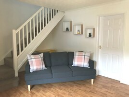 Una sala de estar con un sofá gris, dos almohadas de cuadros, una escalera de madera y tres cuadros en la pared.